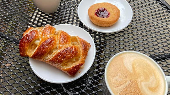 A braided pastry, a jam-filled cookie and a latte on a patio table