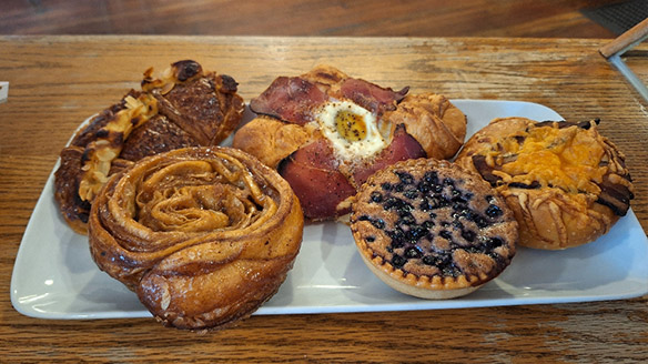 A platter of pastries, including a breakfast bacon croissant, a cinnamon swirl and a blueberry tart